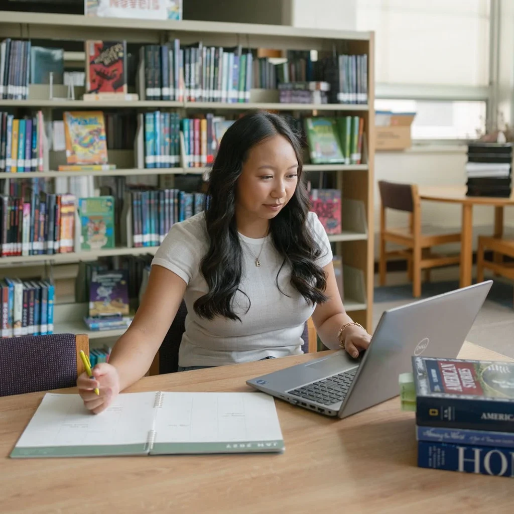 A student studies with a notebook and laptop in the library.