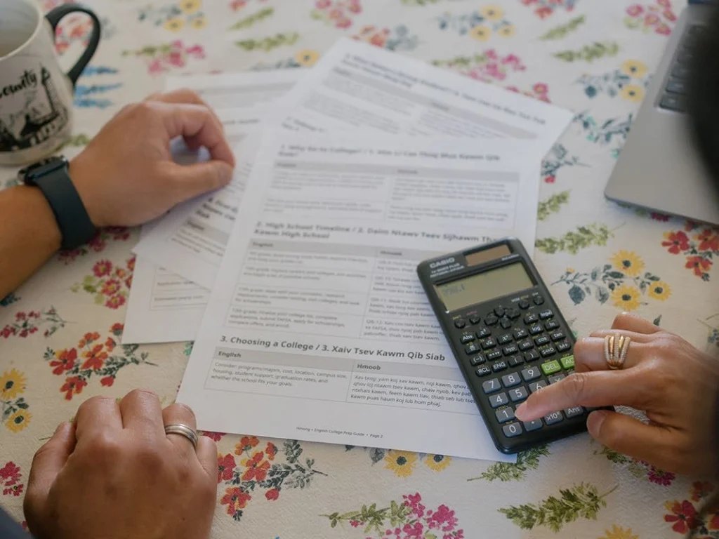 Hands compare financial documents using a calculator.