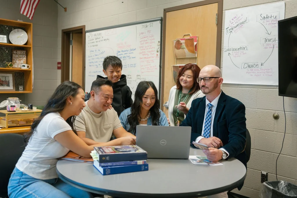 Students and adults gathered around a laptop in a school office.