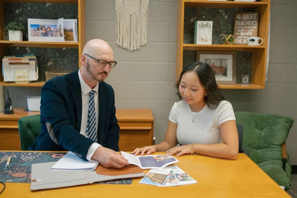A student and an adviser discuss documents at a desk.
