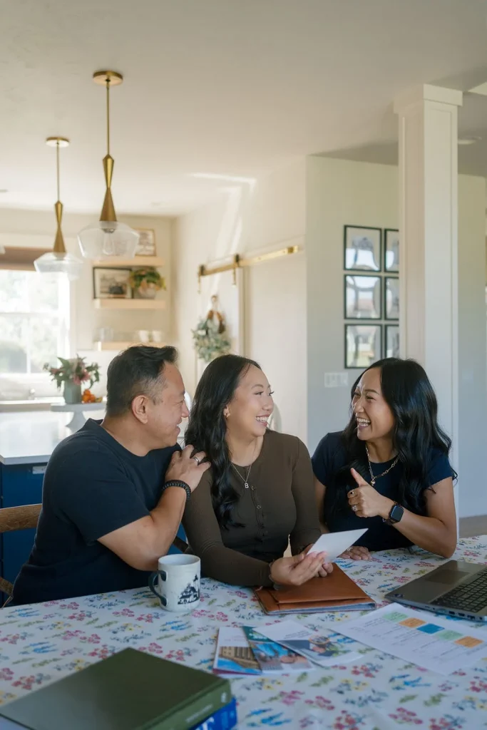 Three people discuss papers at a table at home.