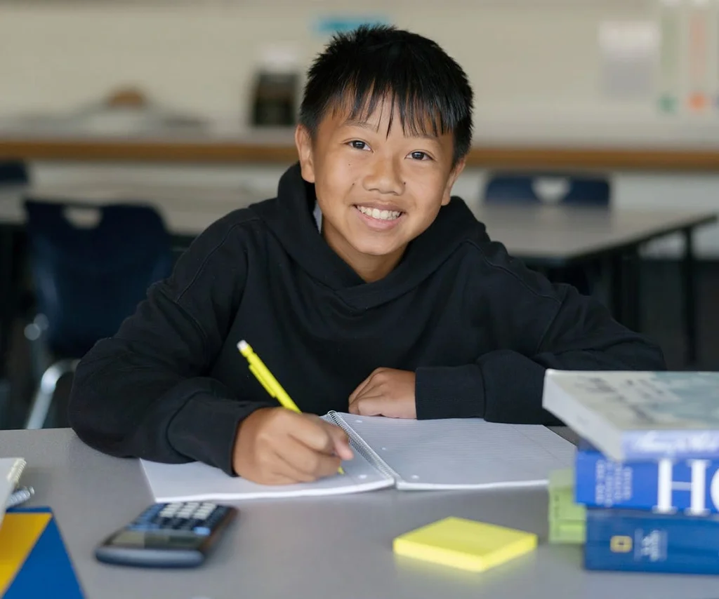 A student writes at a classroom desk.