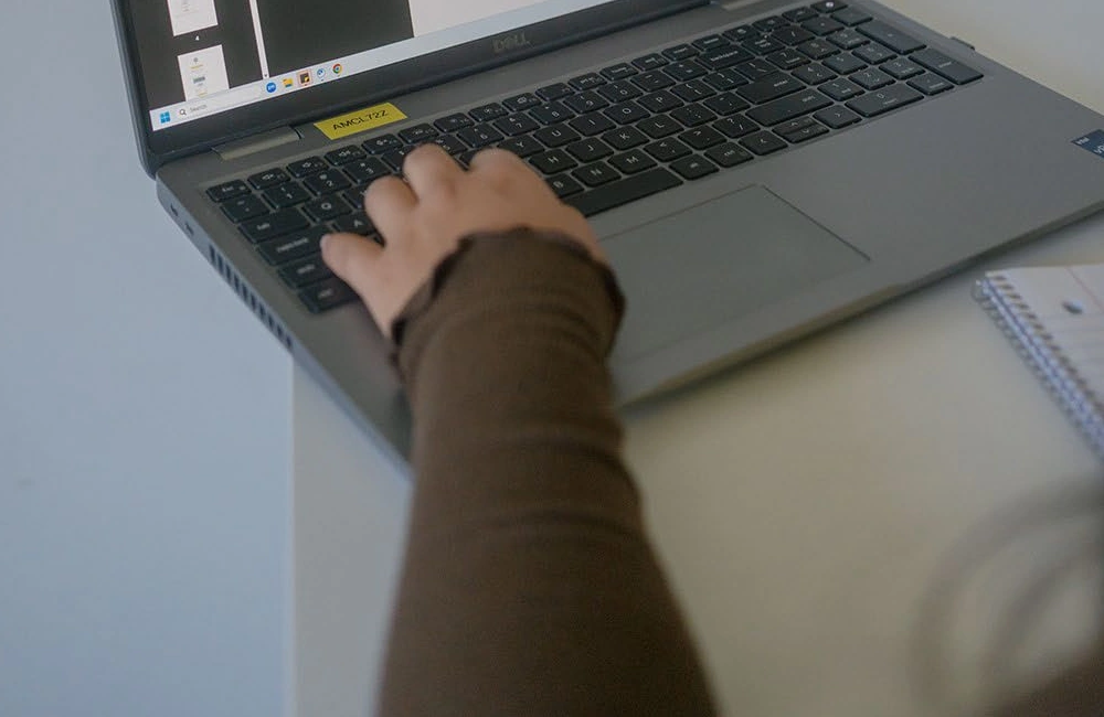 A hand works at a laptop keyboard beside study materials.